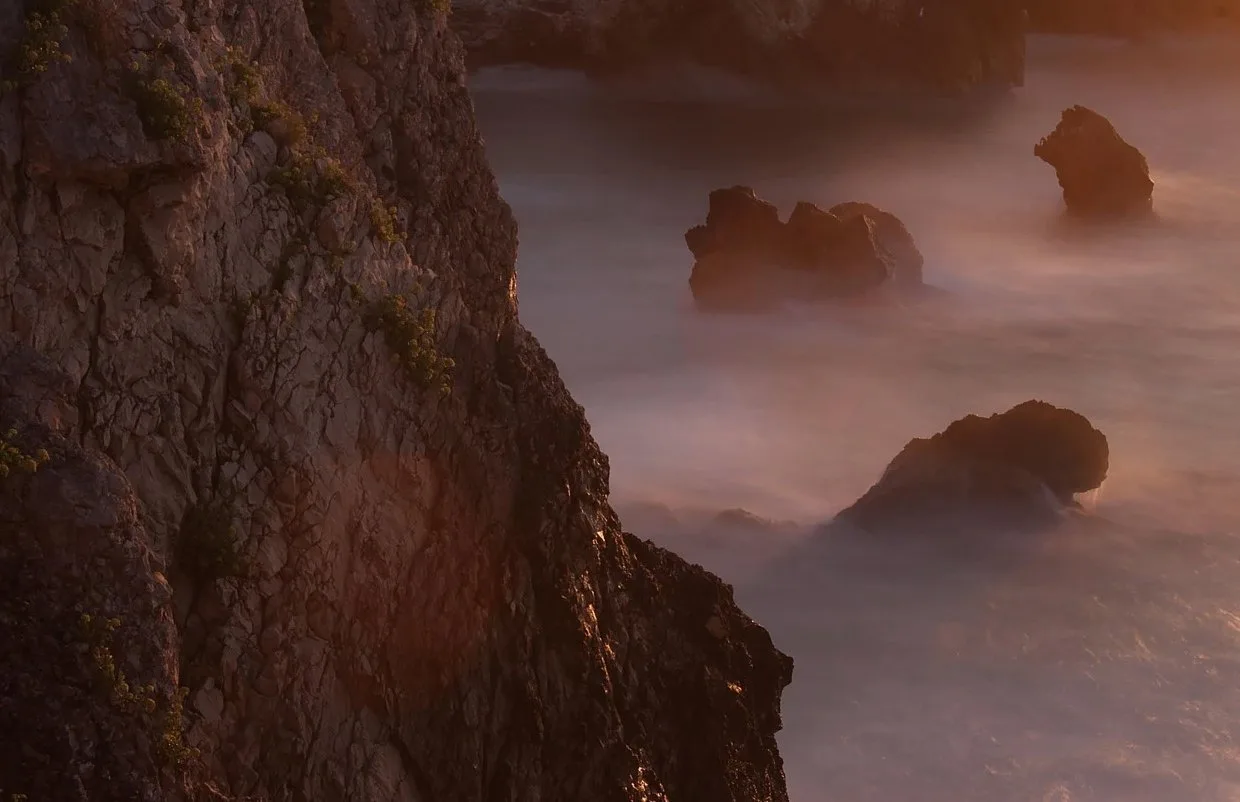 Dark coastal rocks in misty long-exposure surf