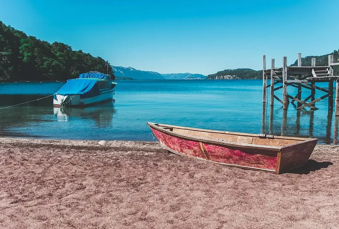 Wooden boat on a sandy beach beside a moored boat on blue water