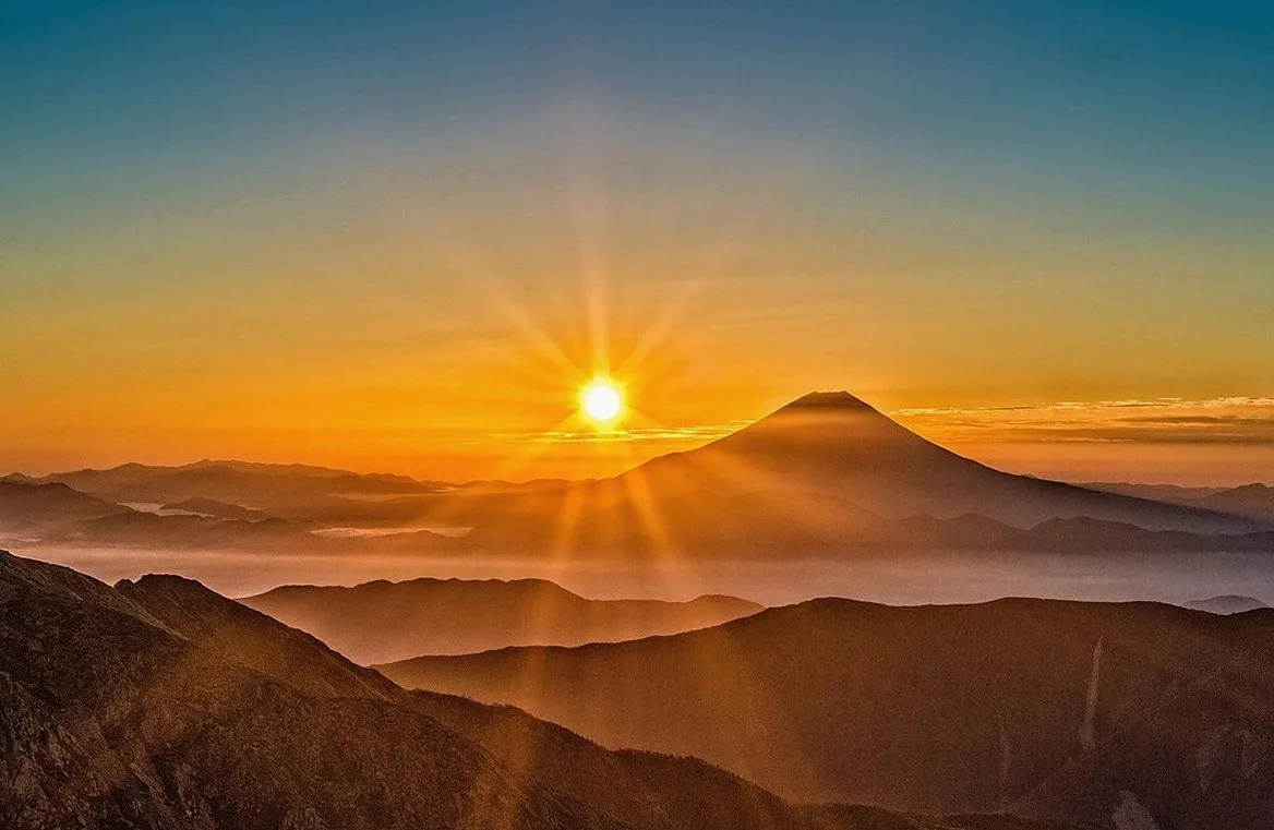 Sun rising behind layered mountain ridges in an orange sky