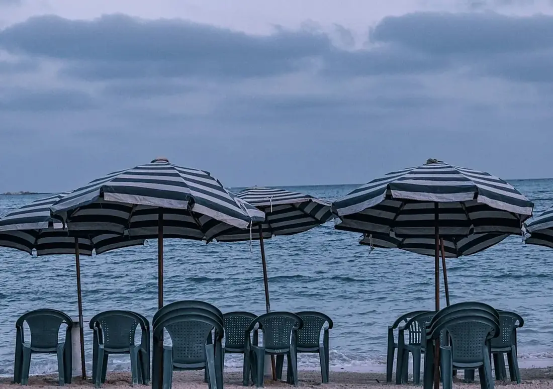 Striped beach umbrellas and plastic chairs facing a grey-blue sea