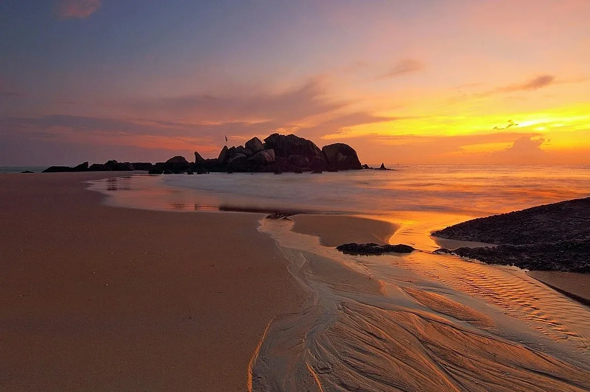 Sunset over a sandy beach with a rocky islet